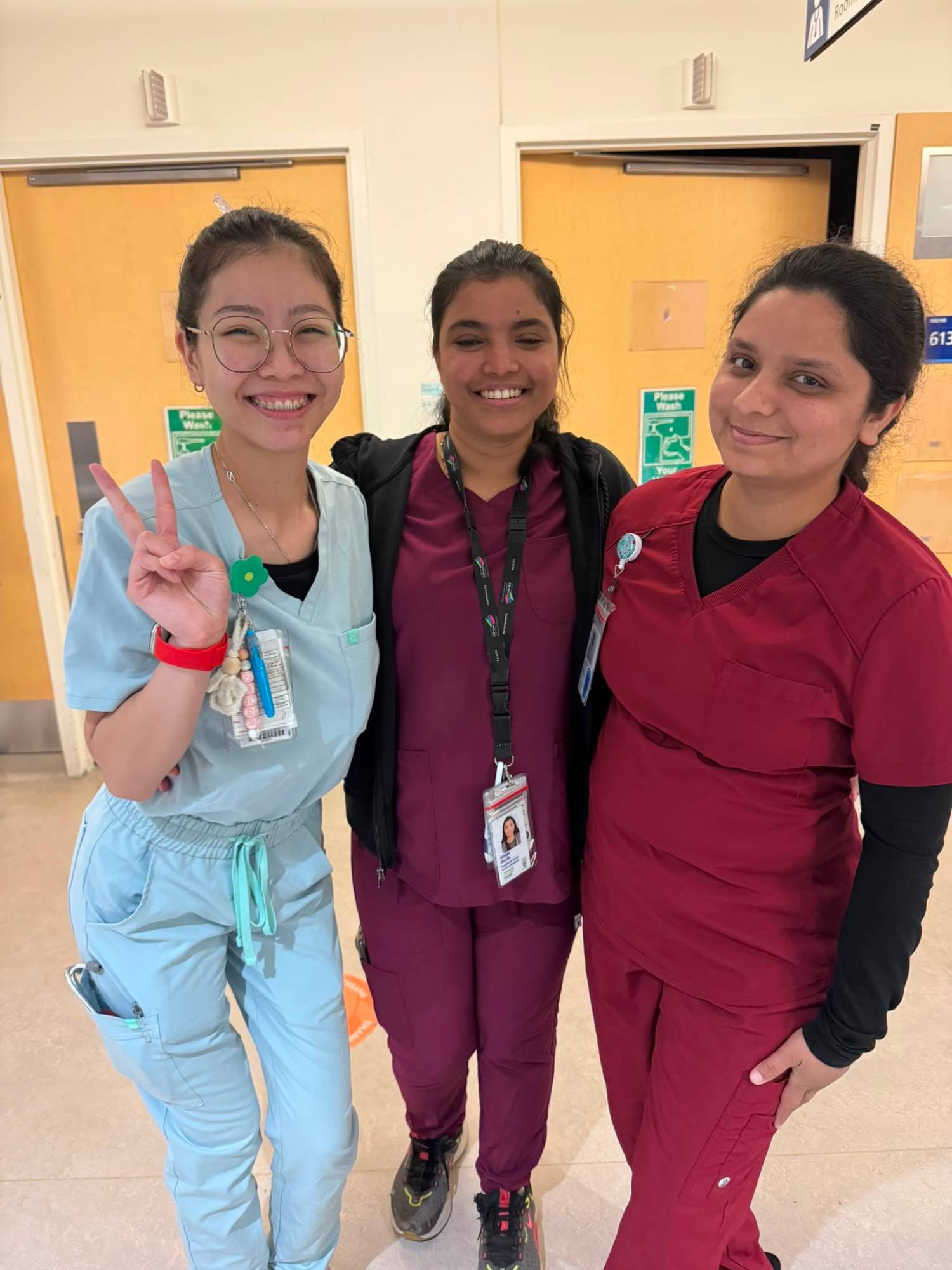 Three team members in scrubs smiling together in a hospital hallway