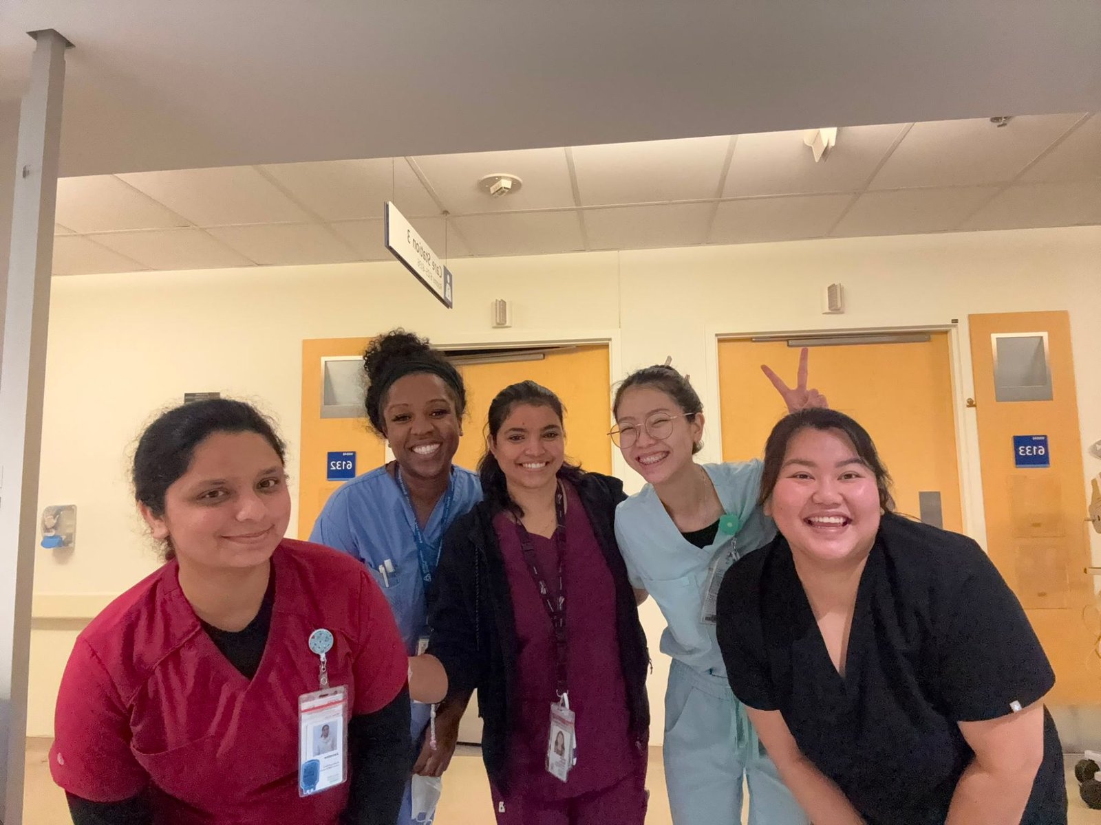 Five team members in scrubs smiling together outside patient rooms